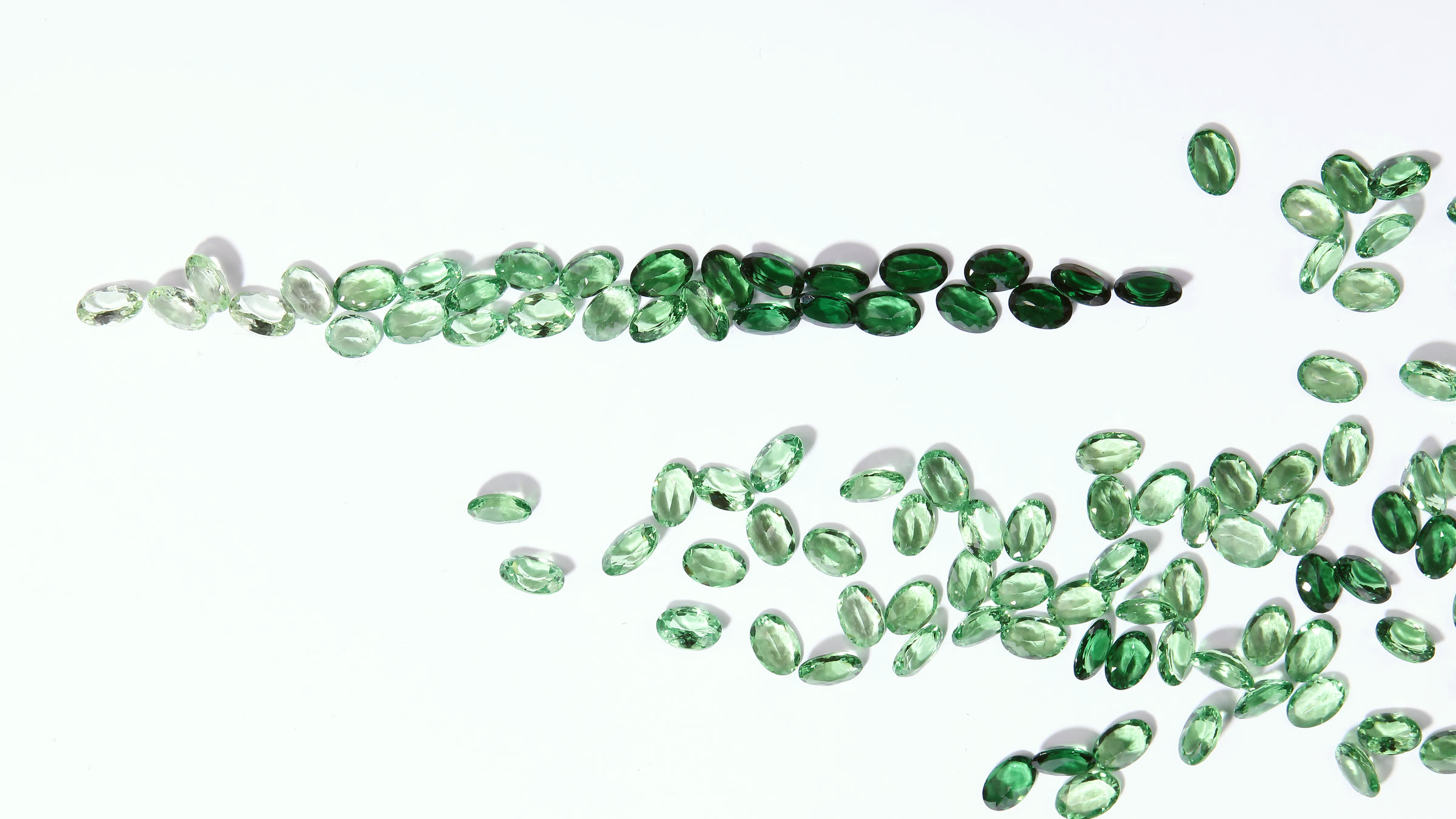 Oval cut green sapphires graded from pale to deep on a pale working surface