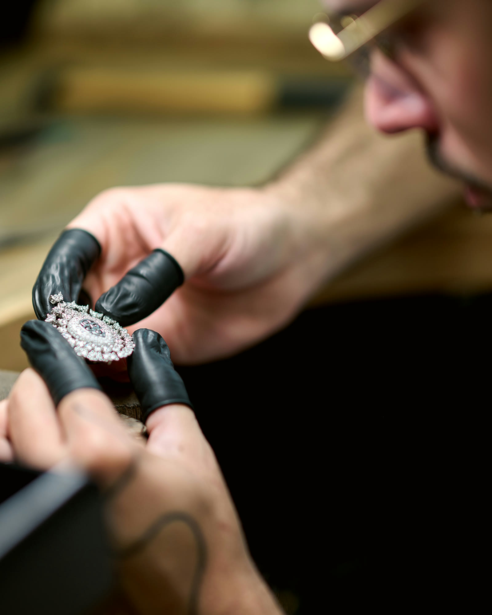 A jeweller with an eye loupe inspecting a diamond-set oval piece held on a shellac stick