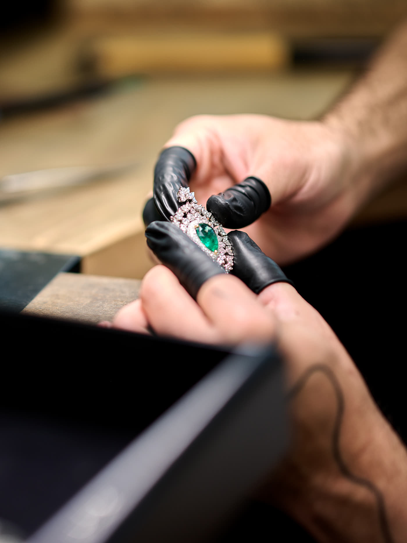 A gloved jeweller holding an emerald and diamond piece at the bench